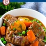 A bowl of slow cooker beef stew featuring beef, potatoes, carrots and peas.