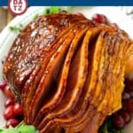 A smoked ham with brown sugar glaze on a platter garnished with herbs.