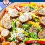 A skillet of sausage and pepper pasta with parsley and parmesan cheese sprinkled on top.