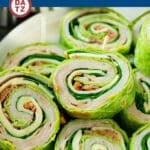 A plate with several turkey roll up sandwiches stacked on each other.