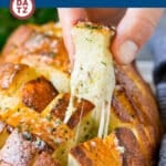 A piece of cheesy pull apart bread being lifted from a loaf of bread.