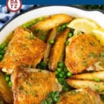 A skillet with Chicken Vesuvio with chicken thighs, potato wedges, peas and sauce.