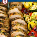 A plate with rows of sliced grilled pork tenderloin and various grilled vegetables.