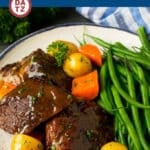 A plate with slow cooker pot roast slices, carrots, potatoes and green beans.